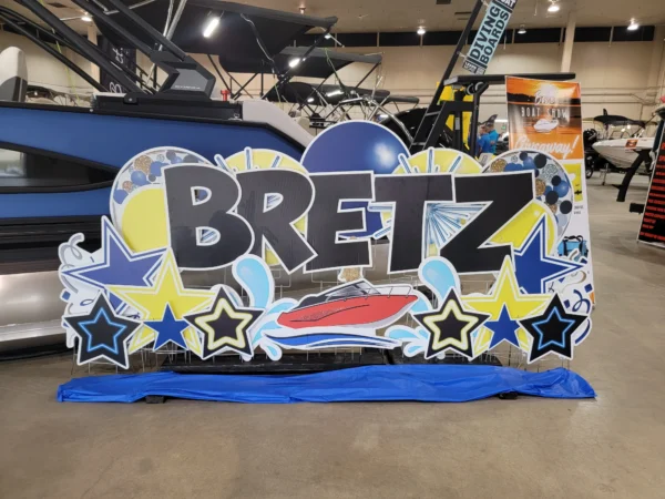 A yard sign that says "BRETZ" in black letters. Colorful graphics surround the sign.
