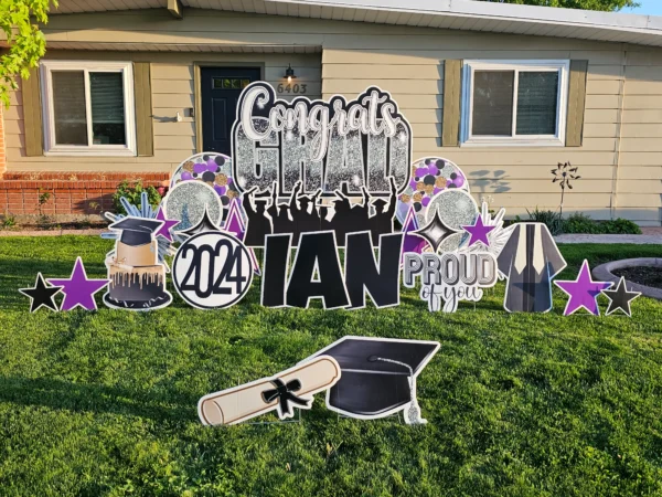 A large yard sign in front of a house that says "Congrats Grad Ian" in colorful letters. Colorful graphics surround the sign.