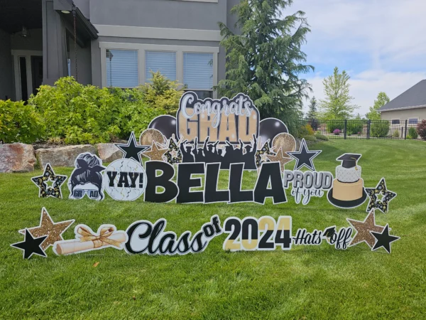 A large yard sign in front of a house that says "Congrats Grad Bella Class of 2024" in colorful letters. Colorful graphics surround the sign.