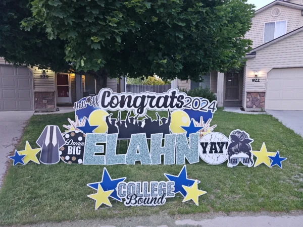 A large yard sign in front of a house that says "Congrats Elahn College Bound" in colorful letters. Colorful graphics surround the sign.