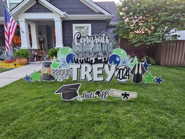 A large yard sign in front of a house that says "Congrats Grad Trey" in colorful letters. Colorful graphics surround the sign.