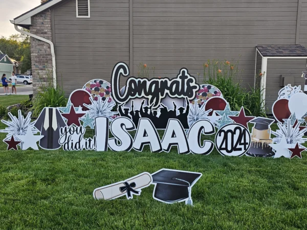 A large yard sign in front of a house that says "Congrats Isaac you did it" in black and white letters. Colorful graphics surround the sign.