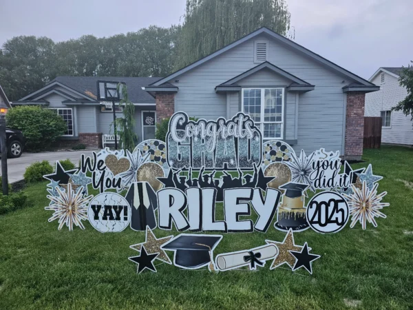 A large yard sign in front of a house that says "Congrats Grad Riley" in colorful letters. Colorful graphics surround the sign.