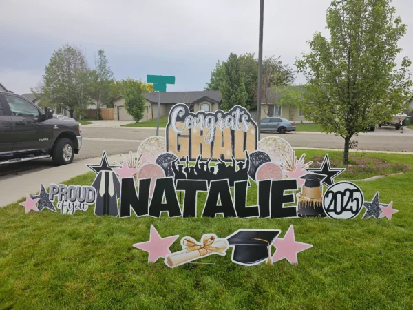 A large yard sign in front of a house that says "Congrats Grad Natalie" in colorful letters. Colorful graphics surround the sign.