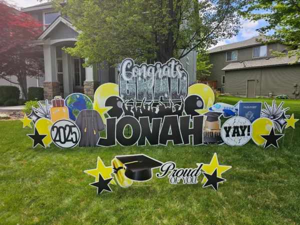 A large yard sign in front of a house that says "Congrats Grad Jonah" in colorful letters. Colorful graphics surround the sign.