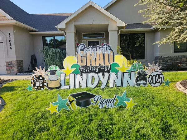 A large yard sign in front of a house that says "Congrats Grad Lindynn" in colorful letters. Colorful graphics surround the sign.