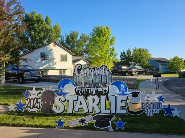 A large yard sign in front of a house that says "Congrats Grad Starlie" in colorful letters. Colorful graphics surround the sign.