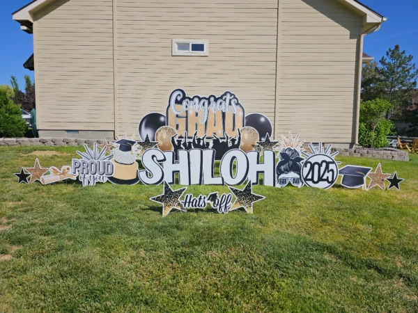 A large yard sign in front of a house that says "Congrats Grad Shiloh" in colorful letters. Colorful graphics surround the sign.