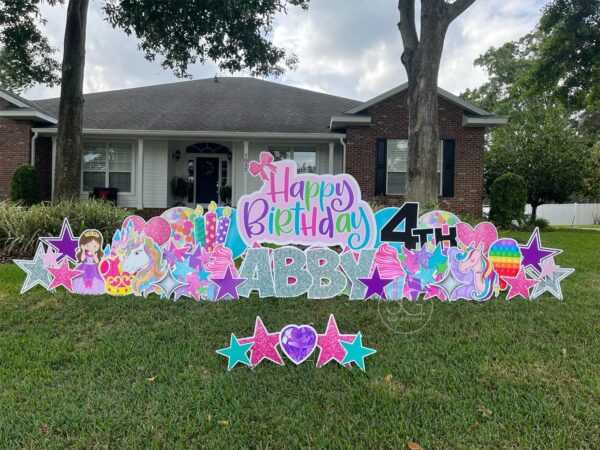 A yard sign in front of house that says "Happy 4th Birthday Abby" in colorful letters. Colorful graphics surround the sign.