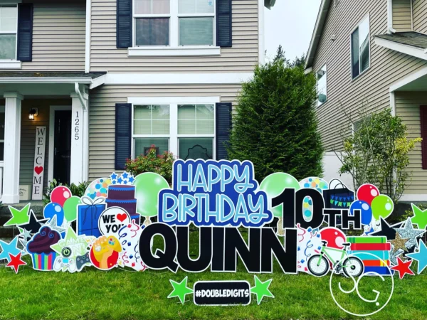 A yard sign in front of house that says "Happy 10th Birthday Quinn" in blue and black letters. Colorful graphics surround the sign.