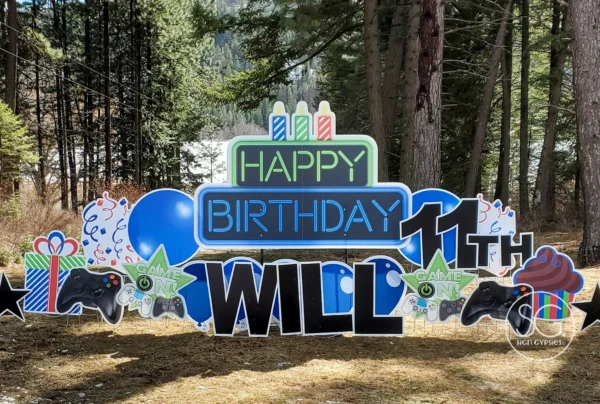 A yard sign in front of trees that says "Happy 11th Birthday Abby" in colorful letters. Colorful graphics surround the sign.