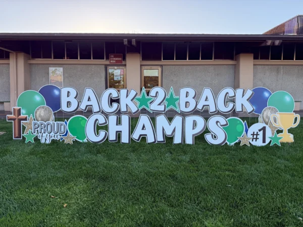 A yard sign in front of building that says "BACK 2 BACK CHAMPS" in white letters. Colorful graphics surround the sign.