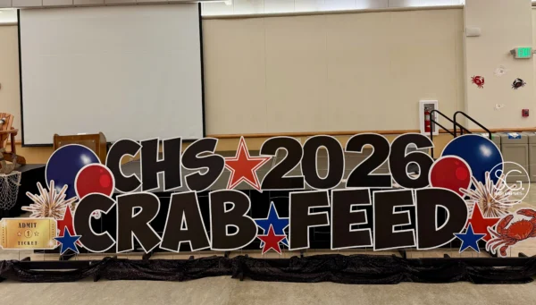 A sign in a large room that says "CHS 2026 CRAB FEED" in black letters. Colorful graphics surround the sign.