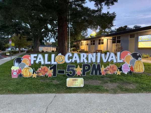 A yard sign in front of building that says "FALL CARNIVAL 1-5 PM" in white and black letters. Colorful graphics surround the sign.