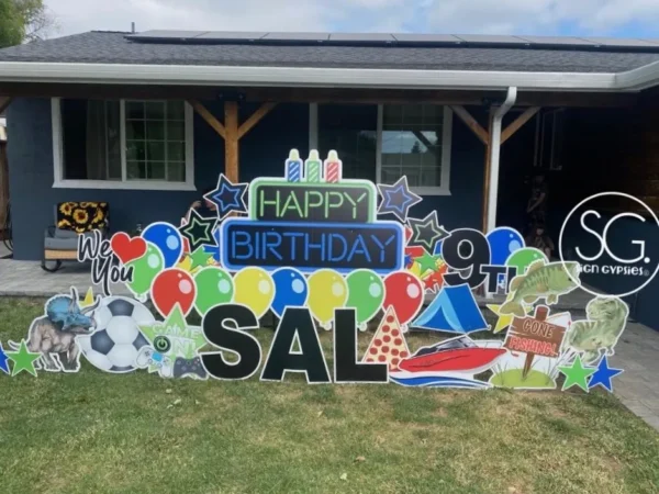 A yard sign in front of a house that says "Happy 9th Birthday Sal". The phrase is surrounded by colorful graphics.