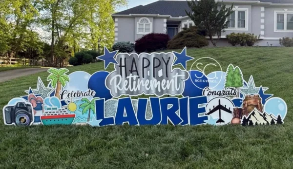 A yard sign in front of a house that says "Happy Retirement Laurie" in colorful letters. The phrase is surrounded by colorful graphics.