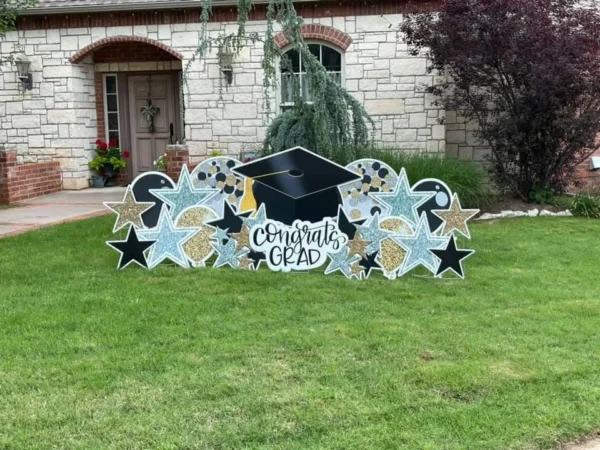 A large yard sign in front of a house that says "Congrats Grad" in black letters. Colorful graphics surround the sign.