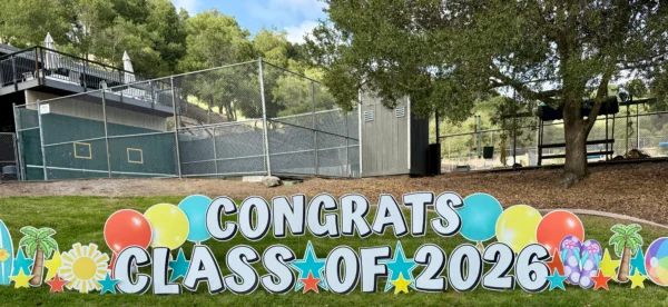 A large yard sign that says "Congrats Class of 2026" in white letters. Colorful graphics surround the sign.