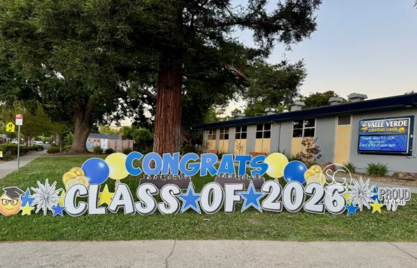 A large yard sign in front of a house that says "Congrats Class of 2026" in black letters. Colorful graphics surround the sign.