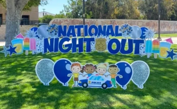 A yard sign that says "NATIONAL NIGHT OUT" in blue letters. Colorful graphics of balloons and children surround the sign.