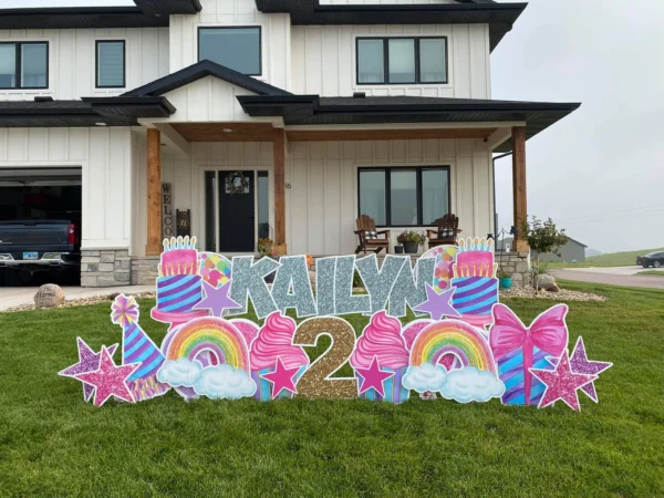 A yard sign in front of a house that says "KAILYN 2". The phrase is surrounded by colorful graphics.