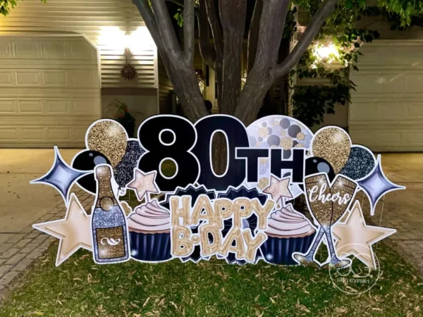 A yard sign in front of a house and tree that says "80th Happy B-Day" in colorful letters. The phrase is surrounded by colorful graphics.