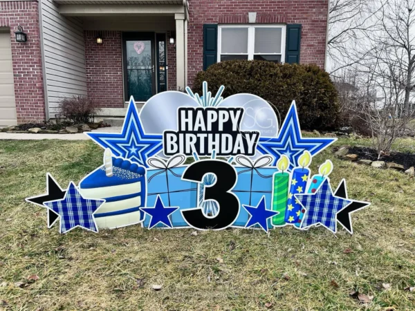 A yard sign in front of a house that says "Happy Birthday 3" in colorful letters. The phrase is surrounded by colorful graphics.
