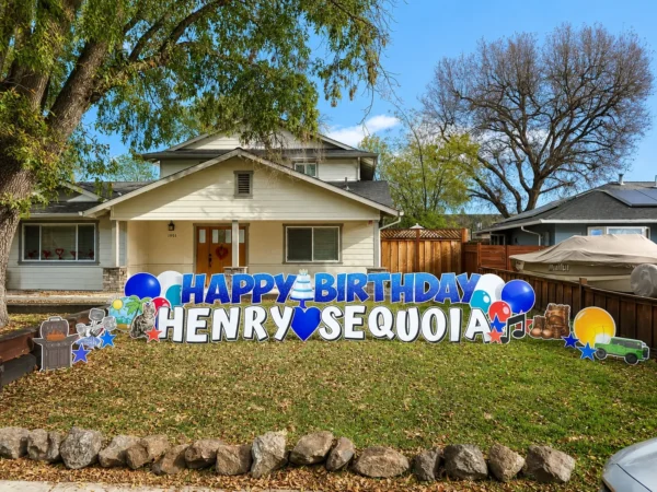 A yard sign in front of a house that says "HAPPY BIRTHDAY HENRY SEQUOIA" in blue and white letters with colorful graphics surrounding it.