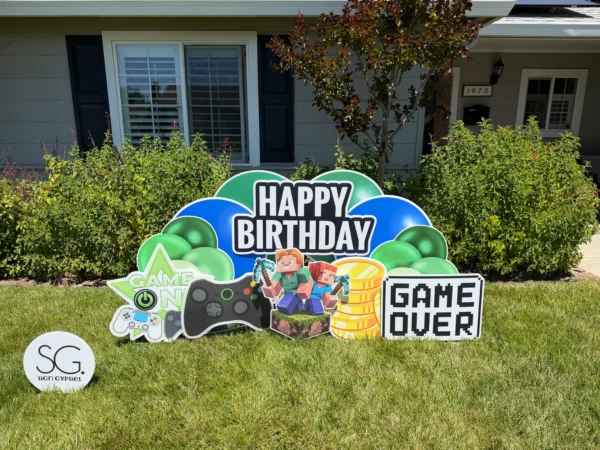 A yard sign in front of a house that says "Happy Birthday" in white letters. The phrase is surrounded by colorful graphics.