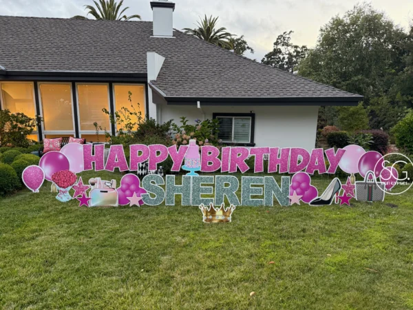 A yard sign in front of a house that says "HAPPY BIRTHDAY SHEREN" in pink and silver letters with colorful graphics around the letters.