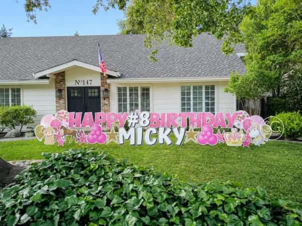 A yard sign in front of a house that says "HAPPY #8 BIRTHDAY MICKY" in pink and white letters with colorful graphics around the letters.