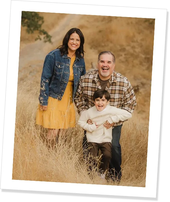 A woman, man, and young boy stand in a field of yellow grass, smiling.