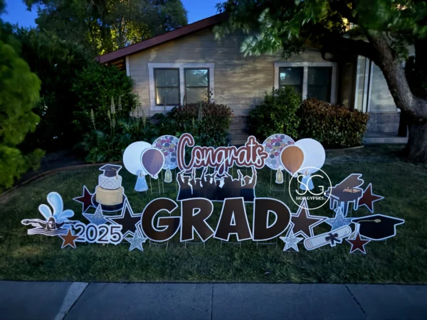 A large yard sign in front of a house that says "Congrats Grad" in black and white letters. Colorful graphics surround the sign.