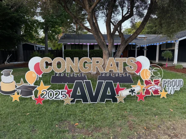 A large yard sign in front of a house that says "Congrats Ava" in black letters. Colorful graphics surround the sign.